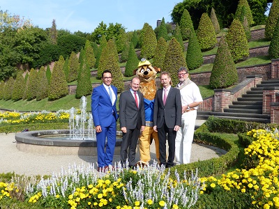Das Team der LAGA GmbH steht mit dem neuen LAGA Maskottchen Kalli im Terassengarten des Kloster Kamp.