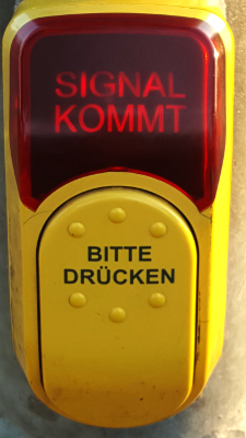 Foto der Ausstellung 'Das Fremde': Anforderungstaster Fußgängerampel mit den Texten 'Signal kommt' und 'bitte drücken'